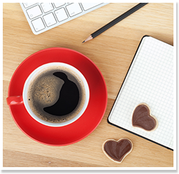 Coffee in a red mug next to keyboard and heart-shaped cookies